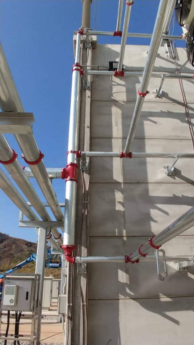Tubulação galvanizada com acoplamentos vermelhos ao longo da estrutura de concreto